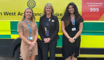 three women standing in front of an ambulance, smiling at the camera