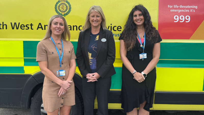 three women standing in front of an ambulance, smiling at the camera