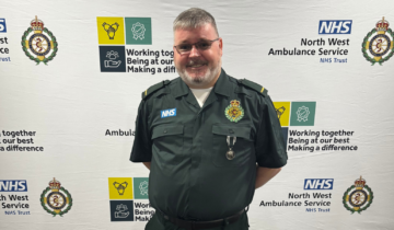 A man stood in front of an NWAS backdrop wearing a green uniform and a medal.