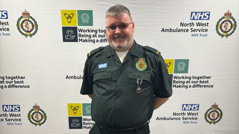A man stood in front of an NWAS backdrop wearing a green uniform and a medal.