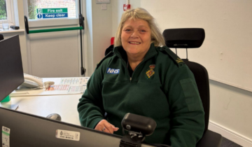 Suzanne sat at a desk smiling in her green uniform