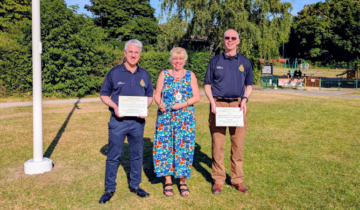 Image of two CFRs with a lady in the middle receiving an award each on a green grassy field.