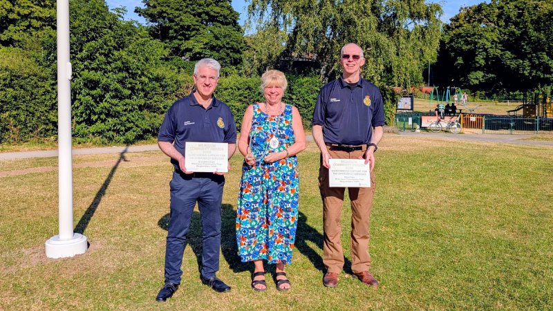 Image of two CFRs with a lady in the middle receiving an award each on a green grassy field.
