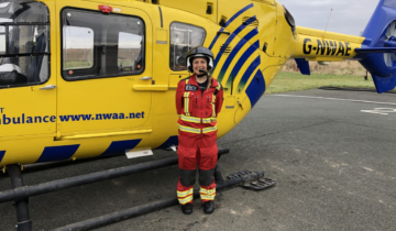 A woman in red uniform wearing a helmet stood in front of a helicopter.