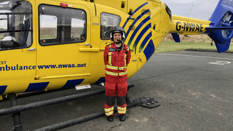 A woman in red uniform wearing a helmet stood in front of a helicopter.