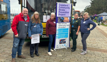 Five people stood in front of a bus next to a banner that says 'Copeland Community Stroke Prevention Project'