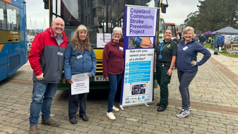 Five people stood in front of a bus next to a banner that says 'Copeland Community Stroke Prevention Project'