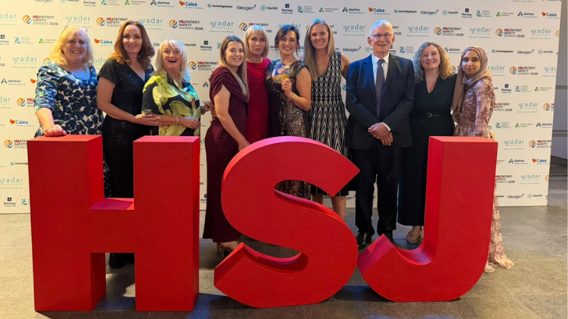 The MAMAS Team stand infront of large red HSJ letters at an awards ceremony.