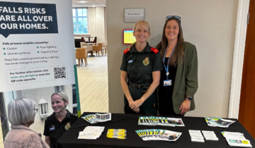 Two people, one in green uniform, the other wearing a blue lanyard stood behind a falls prevention stall.