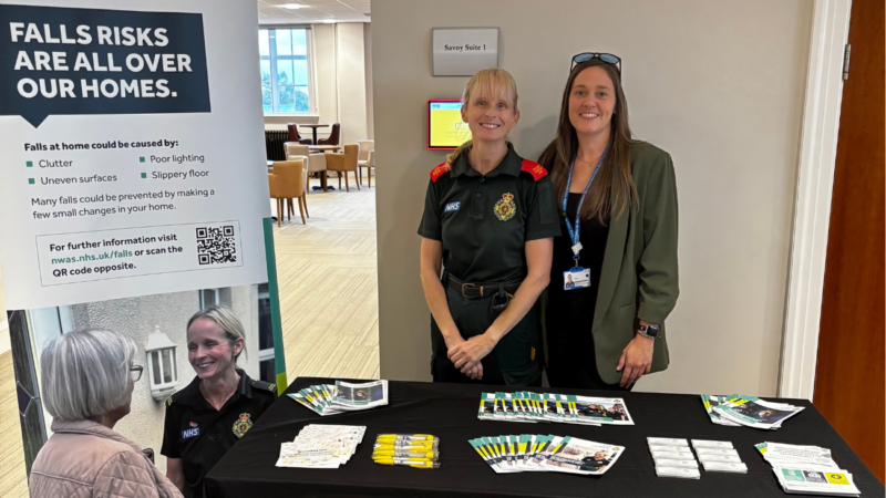 Two people, one in green uniform, the other wearing a blue lanyard stood behind a falls prevention stall.