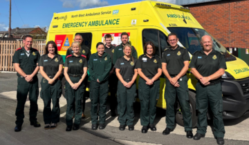 Group of ambulance staff standing in front of an ambulance and smiling at the camera