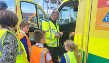 Group of primary school children wearing high-vis jackets stood near front door of ambulance