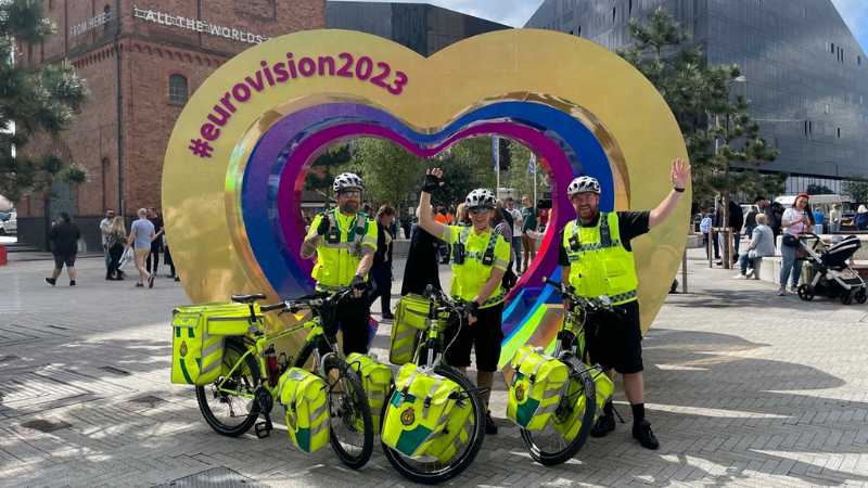 Three paramedics on bikes in front of Eurovision sign